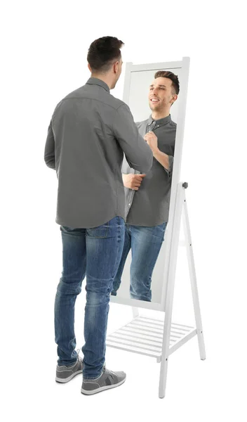 Jonge man kijkend naar zichzelf in de spiegel op witte achtergrond — Stockfoto