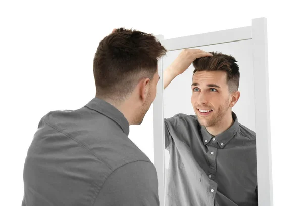 Junger Mann sieht sich selbst im Spiegel auf weißem Hintergrund an — Stockfoto