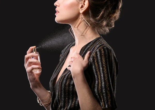 Schöne junge Frau mit einer Flasche Parfüm auf schwarzem Hintergrund — Stockfoto