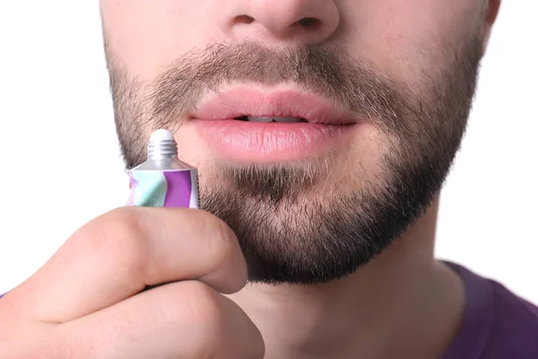 Hombre joven aplicando crema de herpes labial sobre los labios sobre fondo blanco, primer plano — Foto de Stock