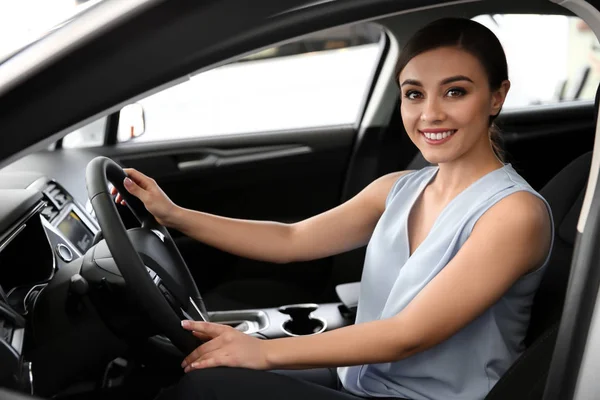 Młoda kobieta siedzi w siedzenie kierowcy nowego samochodu w salonie — Zdjęcie stockowe