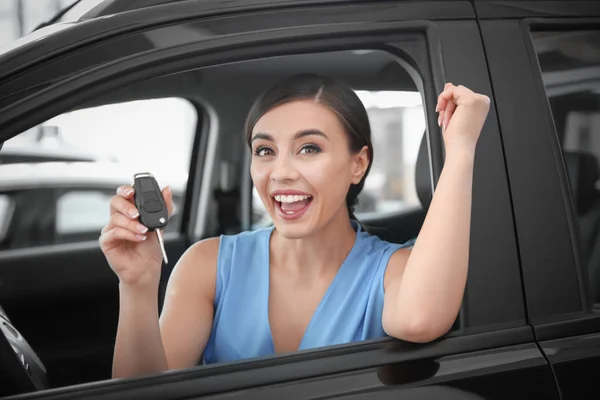 Fiatal nő, kulcsfontosságú ül a vezetőülés új autót szalon — Stock Fotó