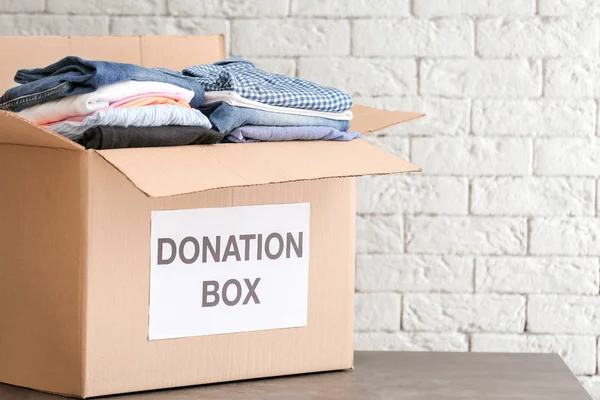 Spendenbox mit Kleidung auf Tisch gegen Ziegelwand — Stockfoto
