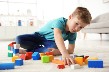 Little autistic boy playing with cubes at home clipart