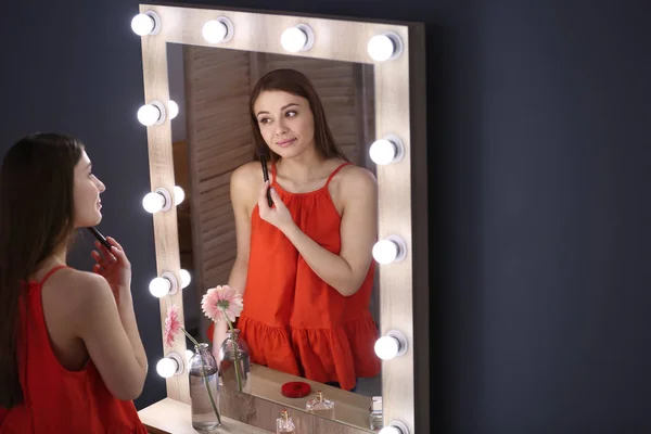 Mooie jongedame toepassing van make-up in de buurt van spiegel — Stockfoto