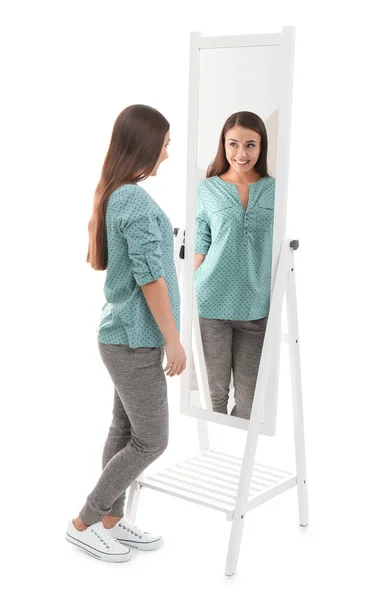 Молодая женщина смотрит на свое отражение в зеркале на белом фоне — стоковое фото