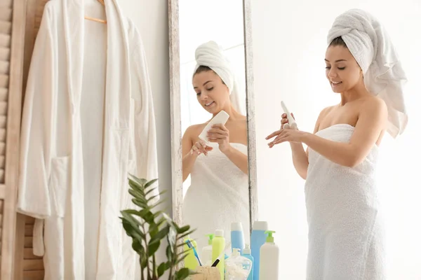 Ung kvinna tillämpa kroppskräm som nära spegeln i badrummet — Stockfoto