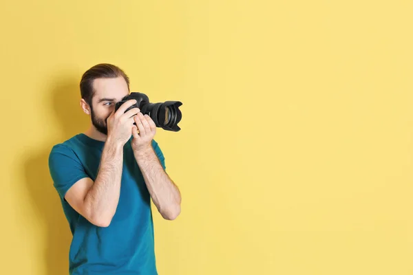 Junger Fotograf mit professioneller Kamera auf farbigem Hintergrund — Stockfoto