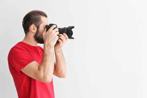 Junger Fotograf mit professioneller Kamera auf weißem Hintergrund — Stockfoto