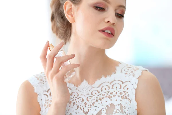Mooie jonge bruid met fles parfum op onscherpe achtergrond, close-up — Stockfoto
