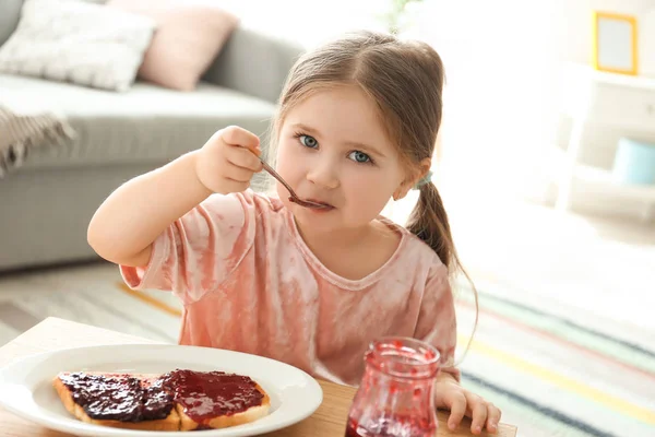 Little girl eating jam at table in living room