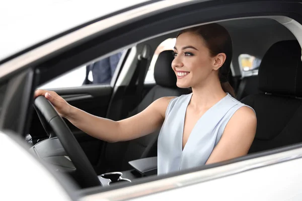 Jovem mulher sentada no assento do motorista do carro novo no salão — Fotografia de Stock