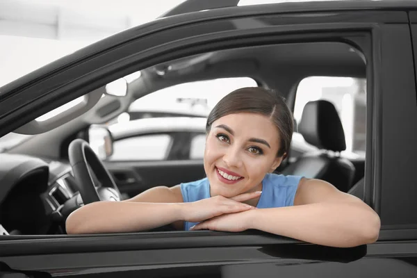 Mujer joven sentada en el asiento del conductor del coche nuevo en el salón — Foto de Stock