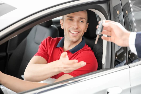 Vendedor pasando la llave al joven en auto en el concesionario. Compra de coche nuevo — Foto de Stock