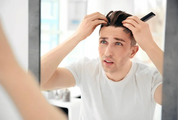 Jeune homme avec problème de perte de cheveux regardant dans le miroir à l'intérieur — Photo