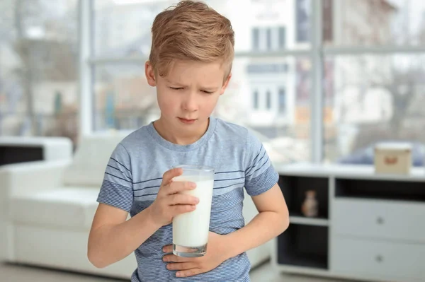 Mały chłopiec z alergią mlecznych trzymając szklankę mleka w pomieszczeniu — Zdjęcie stockowe