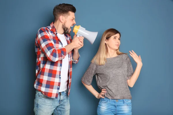 Jonge man met een megafoon schreeuwen op de vrouw op kleur achtergrond — Stockfoto