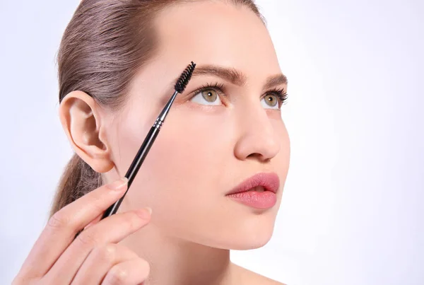 Beautiful woman with perfect eyebrows applying makeup on light background — Stock Photo, Image