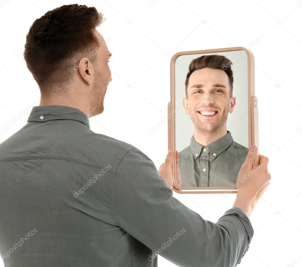 Young man holding mirror and looking at himself on white background