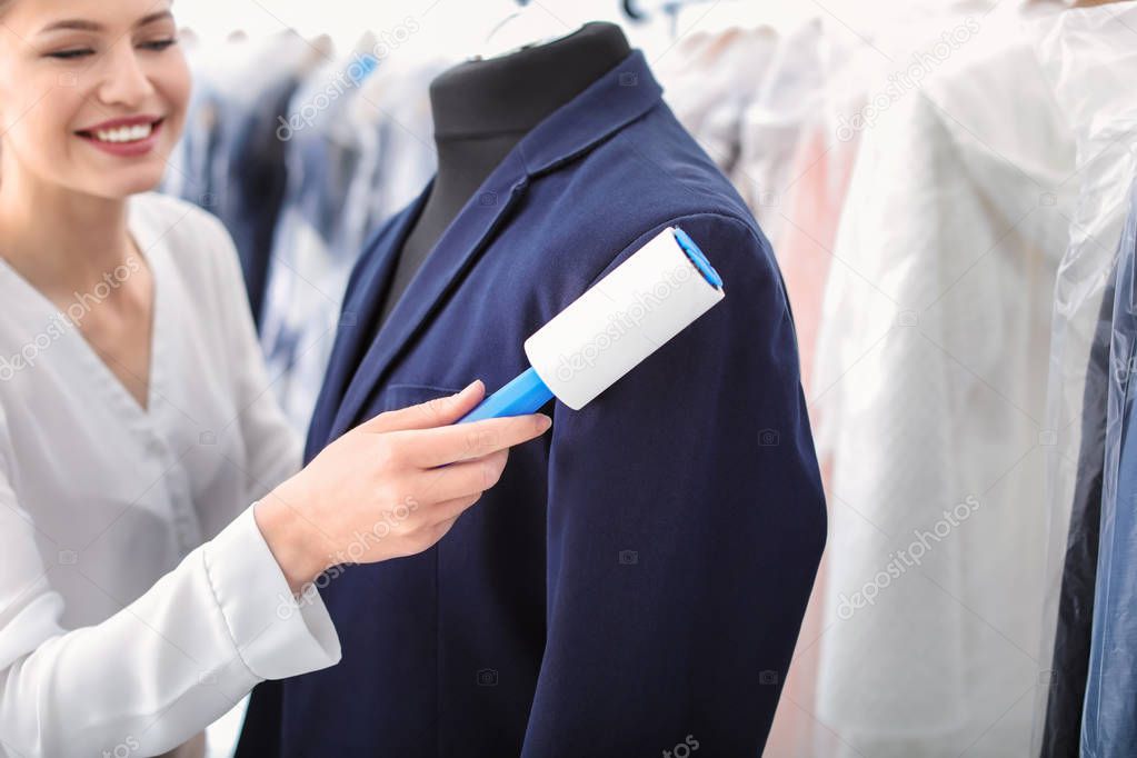 Young woman removing dust from jacket with lint roller at dry-cleaner's