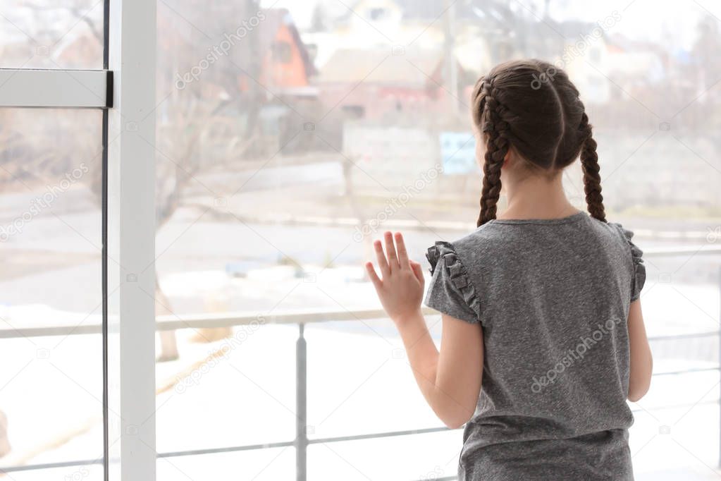 Lonely little girl near window indoors. Child autism