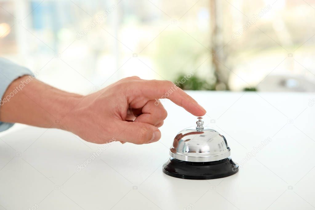Young man ringing service bell on reception desk in hotel, closeup