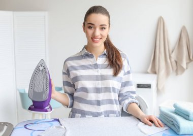 Evde çamaşır ütüleyen genç bir kadın.
