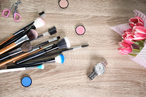 Lägenheten låg sammansättning med professionella borstar, makeup-produkter och tulpaner på trä bakgrund — Stockfoto