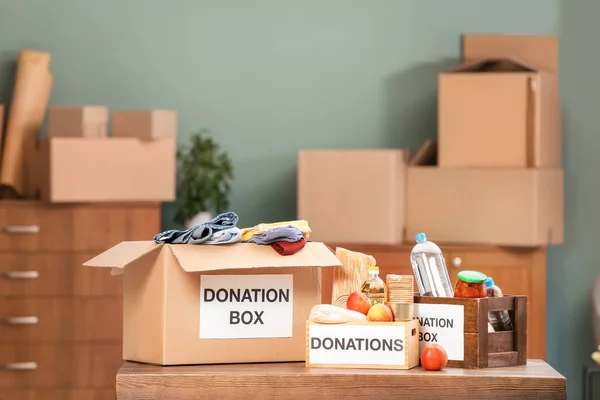 Cajas de donaciones con productos alimenticios y ropa en la mesa en interiores —  Fotos de Stock