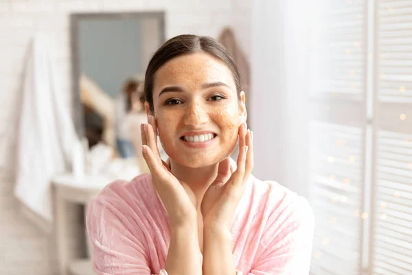 Молодая женщина нанесла естественный скраб на лицо в ванной комнате — стоковое фото