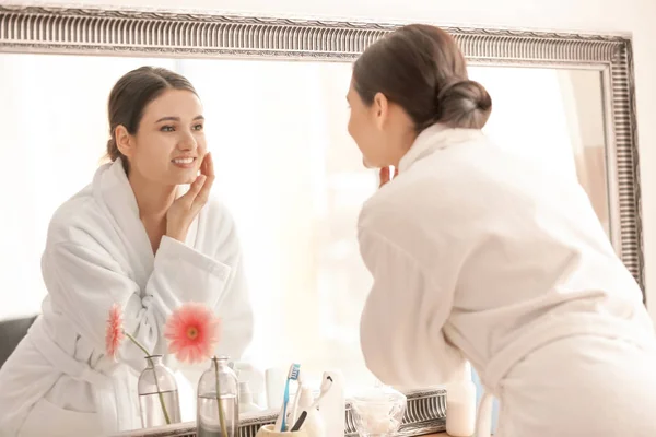 Красивая молодая женщина смотрит на себя в зеркало в помещении — стоковое фото