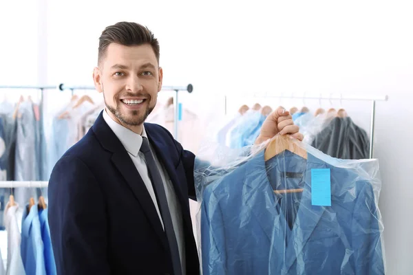 Joven hombre de negocios sosteniendo percha con chaqueta en bolsa de plástico en la tintorería — Foto de Stock