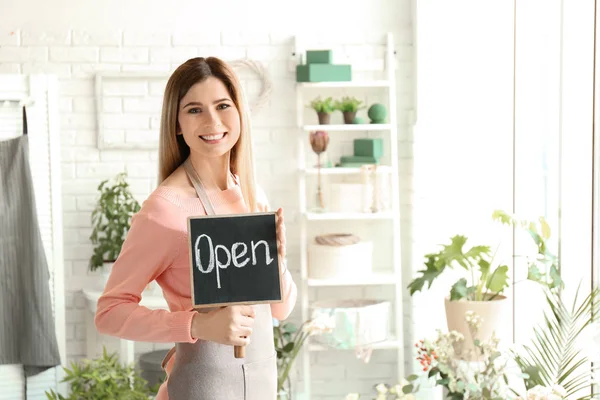 Floristería femenina sosteniendo signo OPEN en el lugar de trabajo — Foto de Stock