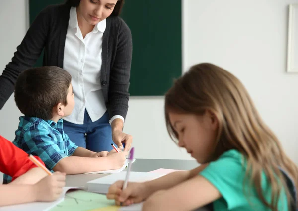 Guru perempuan membantu anak laki-laki dengan tugasnya di kelas di sekolah — Stok Foto