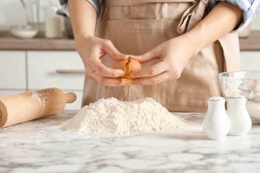 Kadın mutfakta masada un yığını üzerinde yumurta kırma