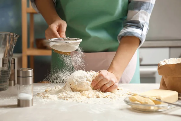 Mujer rociando la harina sobre la masa en la mesa en la cocina —  Fotos de Stock