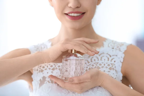 Bella giovane sposa con bottiglia di profumo su sfondo chiaro, primo piano — Foto Stock