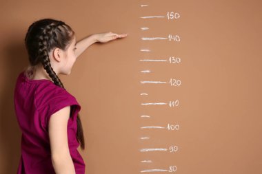 Little girl measuring her height on color background clipart