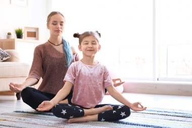 Genç anne ve kızı evde yoga uygulamak