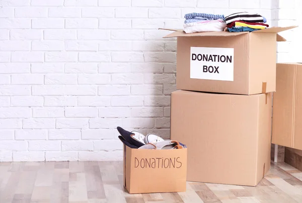 Cajas de donación con zapatos y ropa en el suelo en interiores — Foto de Stock