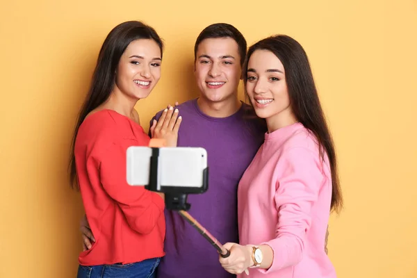 Jovens amigos felizes tomando selfie contra fundo de cor — Fotografia de Stock