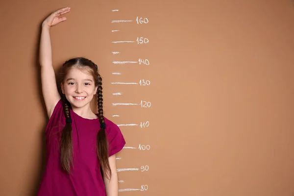 Маленькая девочка измеряет свой рост на цветном фоне — стоковое фото