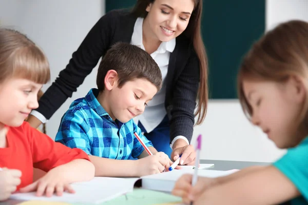 Guru perempuan membantu anak laki-laki dengan tugasnya di kelas di sekolah — Stok Foto