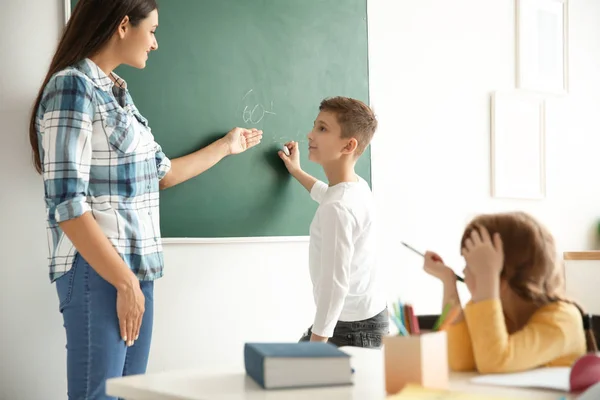 Young teacher and boy near chalkboard in classroom — Stock Photo, Image