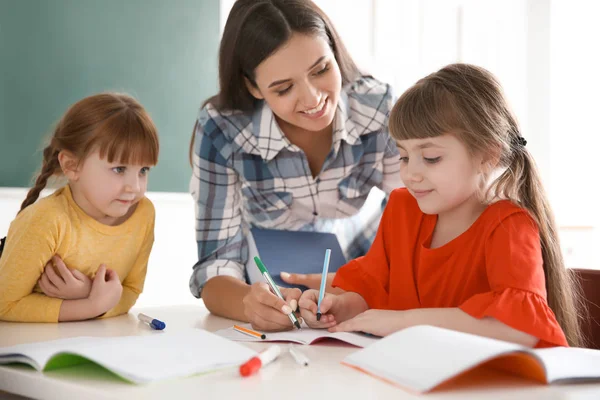 Vrouwelijke leraar meisje helpen met haar taak in klas op school — Stockfoto