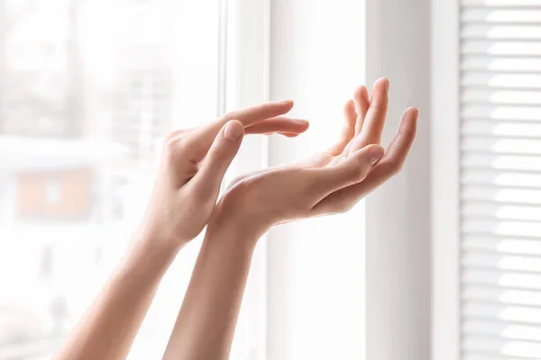 Молодая женщина у окна. Сосредоточьтесь на руках, увлажненных кремом — стоковое фото