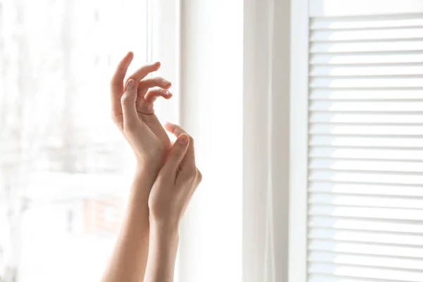 Молодая женщина у окна. Сосредоточьтесь на руках, увлажненных кремом — стоковое фото