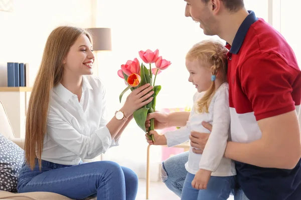 Lycklig kvinna tar emot blommor från make och dotter hemma. Mors dag firande — Stockfoto