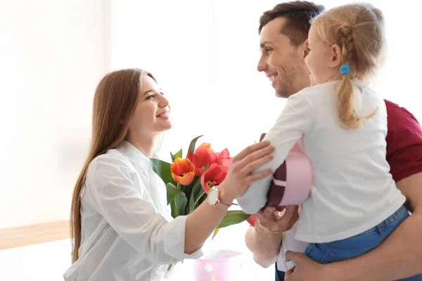 Donna felice che riceve fiori e regali dalla sua famiglia a casa. Festa della mamma celebrazione — Foto Stock