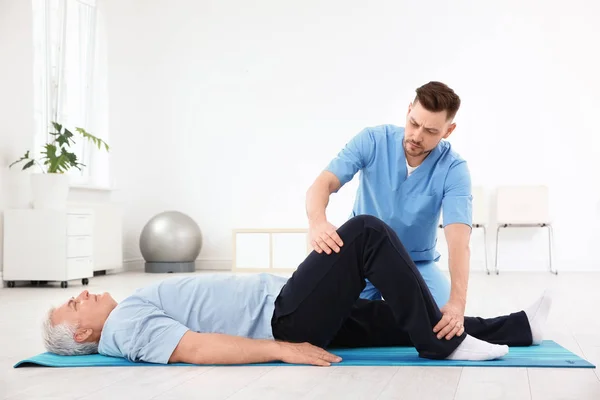 Joven fisioterapeuta trabajando con un paciente mayor en la clínica —  Fotos de Stock